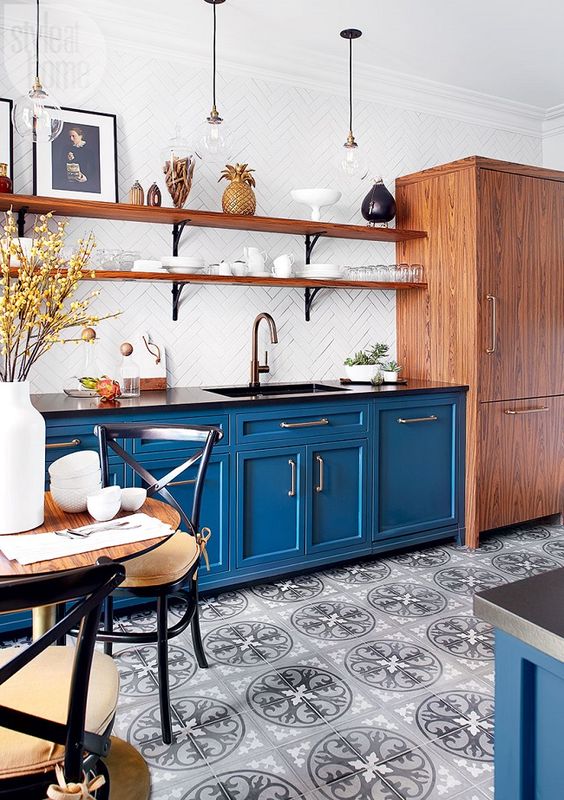 A stylish bistro-inspired kitchen with blue cabinets, a white tile backsplash, black countertops and wooden shelves