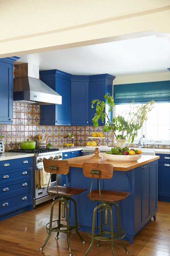 A super bright blue kitchen with a patterned tile backsplash, white countertops and vintage wooden chairs