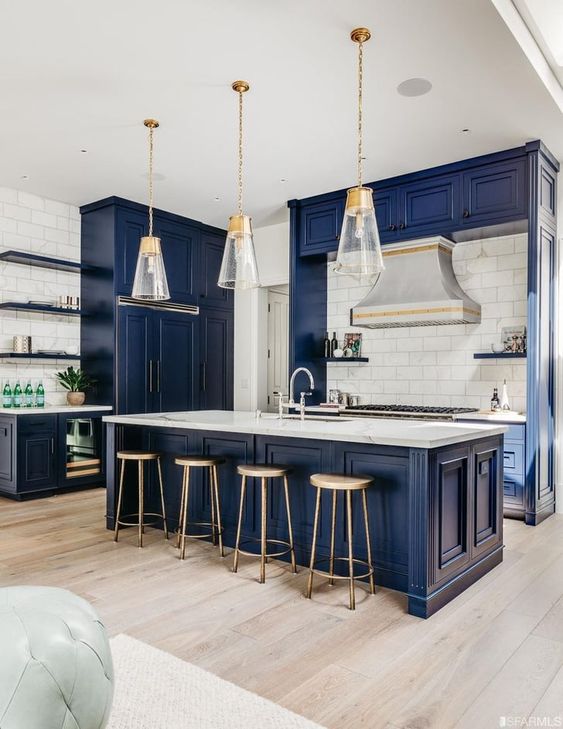 A bold blue vintage-style kitchen with a white tile backsplash, white stone countertops, pendant lamps and wooden stools