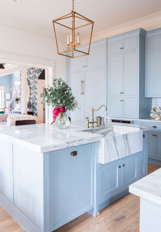 A light blue vintage-style kitchen with a white marble countertop and a brass pendant lamp