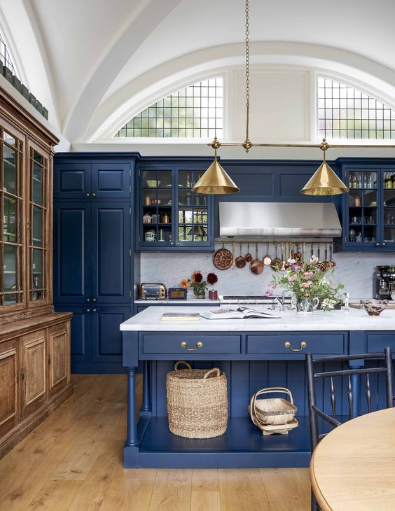 a vintage-inspired kitchen in classic blue with a white marble backsplash and countertops and gold lamps