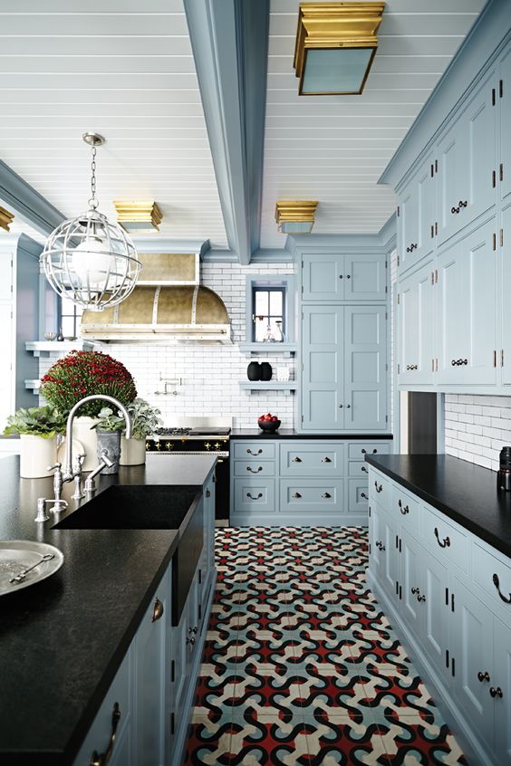 A light blue vintage-style kitchen with black countertops, a white tile backsplash, potted plants and a vintage extractor hood