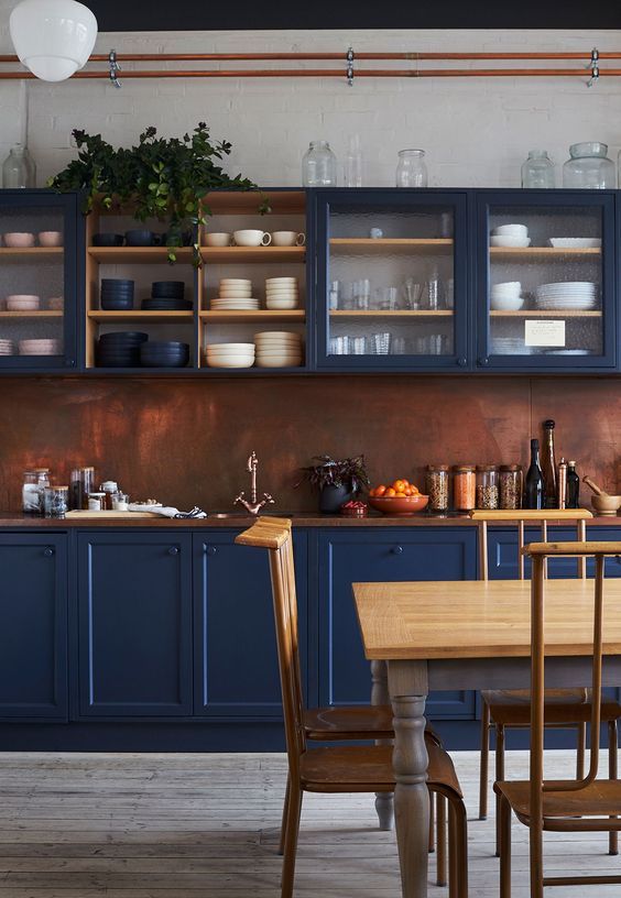 A stunning blue kitchen with a copper backsplash and richly stained wood countertop looks sophisticated and vintage-inspired