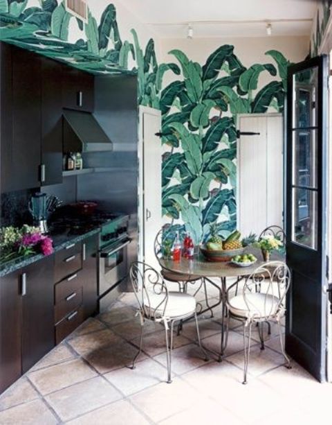 a dark kitchen with bright tropical leaf wallpaper, forged cabinetry and black countertops for a bold look