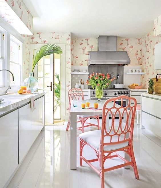 A creative tropical kitchen with flamingo wallpaper, sleek white cabinets, pink rattan chairs and tropical plants