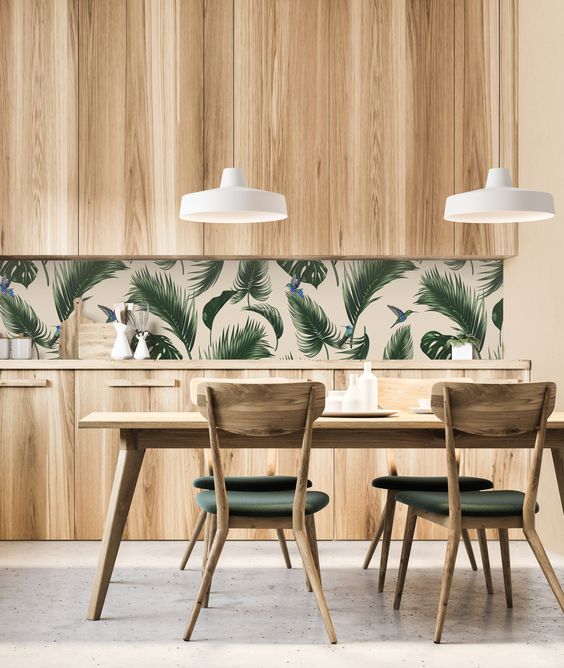 a simple and laconic tropical kitchen with plywood cabinets, a splashback made of tropical leaves, a wooden table and upholstered chairs