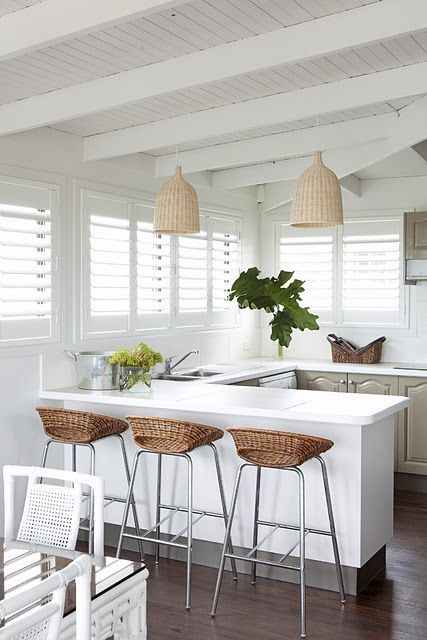A gray and white tropical kitchen with wicker lampshades, wicker stools, gray cabinets and tropical plants
