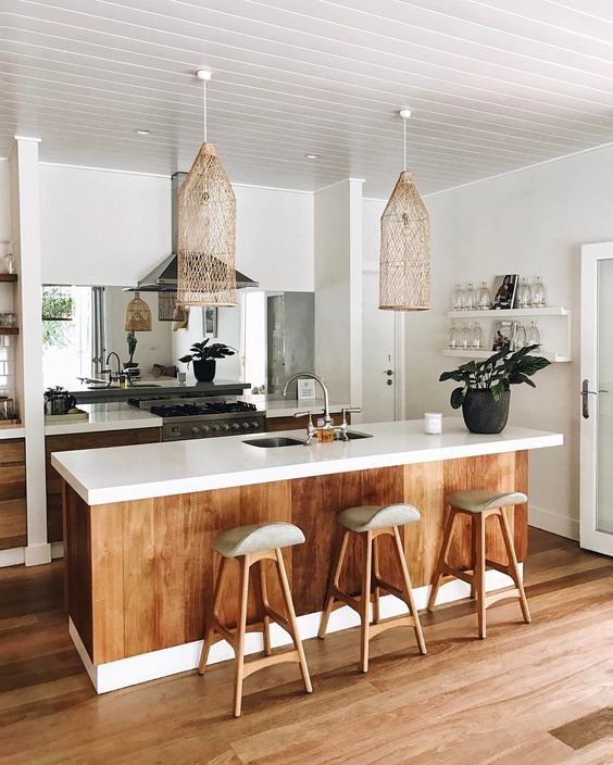 a tropical kitchen with white cabinets, stained wood on the island, wooden stools, wicker lamps and a mirrored backsplash