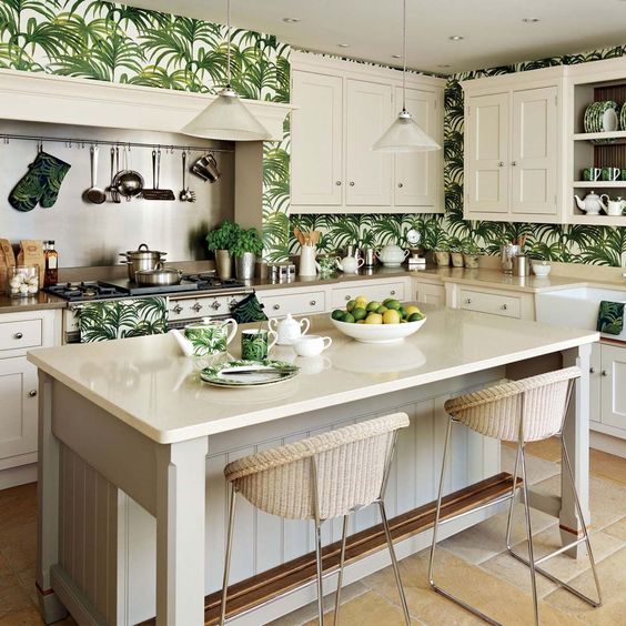 a vintage-inspired tropical kitchen with cream cabinets and tropical leaf wallpaper on the wall, as well as wicker stools