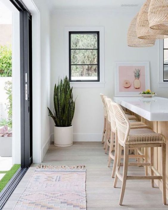 a white tropical kitchen with rattan stools, wicker pendant lamps and a tropical plant in a pot
