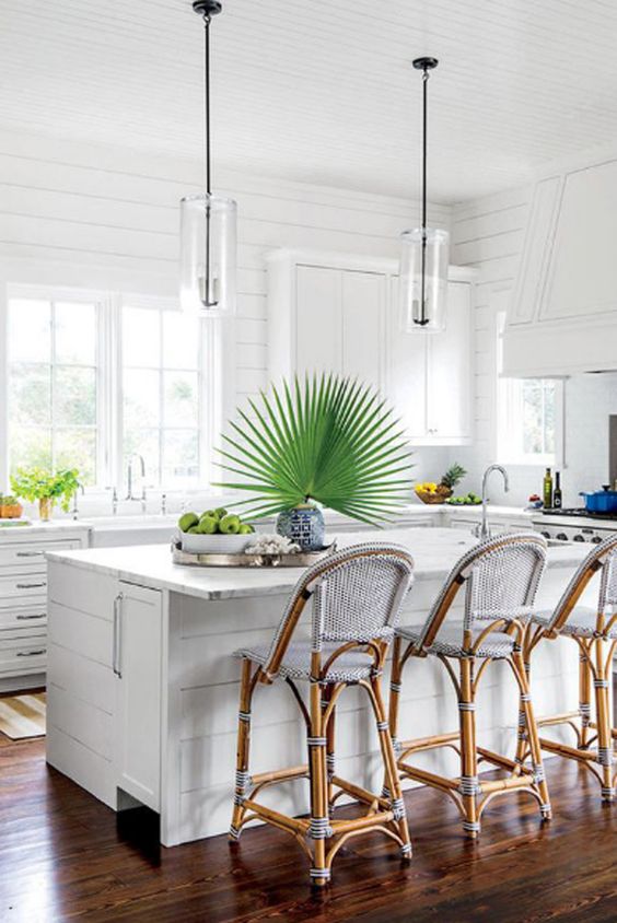 a white tropical kitchen with tropical plants, rattan chairs with blue upholstery and a modern flair