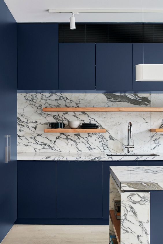 a minimalist navy blue kitchen with a neutral marble backsplash, open shelving and a chic kitchen island