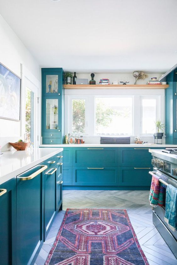 a beautiful blue kitchen with lots of natural light, gold accents and white countertops and a backsplash