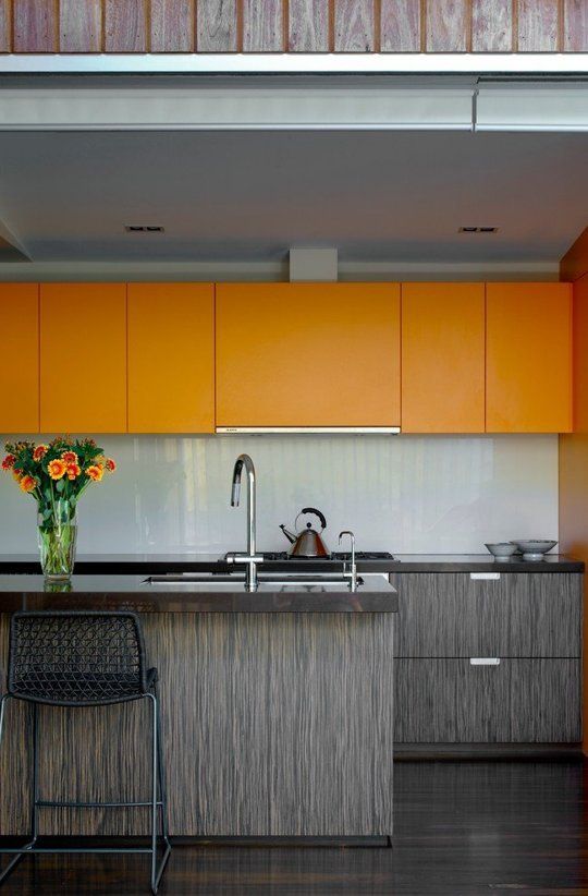 A bold, minimalist kitchen with orange sleek upper cabinets and grayish lower cabinets, plus a white tile backsplash to refresh