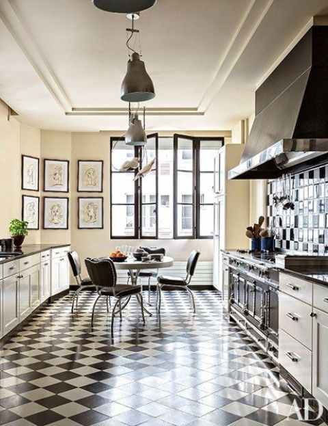 A striking black and white kitchen with tiled floors, tiled splashback, black chairs and a round table and metal hanging lamps