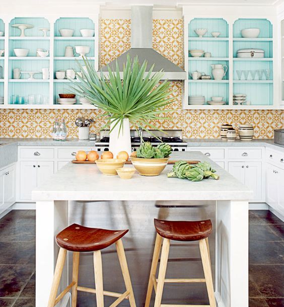a bright tropical kitchen with yellow mosaic tiles, blue cabinets, tropical plants and leather and wooden stools
