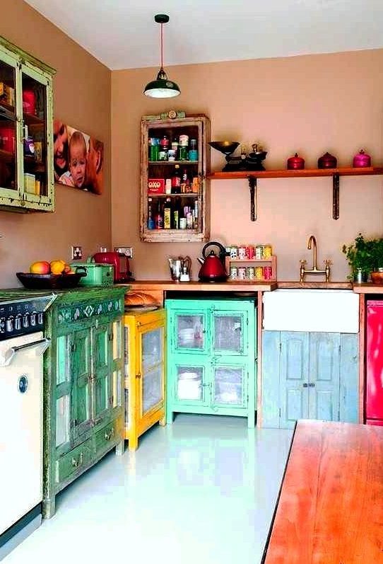 A maximalist boho kitchen with dusty pink walls, colorful mismatched cabinets, and colorful cookware is fantastic