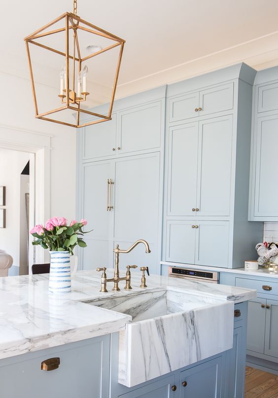 Serenity blue kitchen cabinets with white marble countertops and brass accents for a retro look
