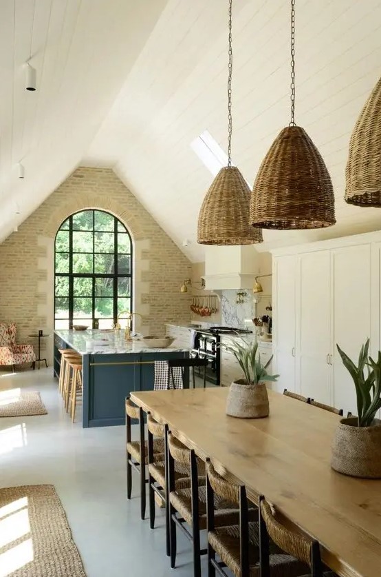 a barn kitchen with a stone accent wall, arched window, white shaker-style cabinets, stone blue kitchen island and woven pendant lamps