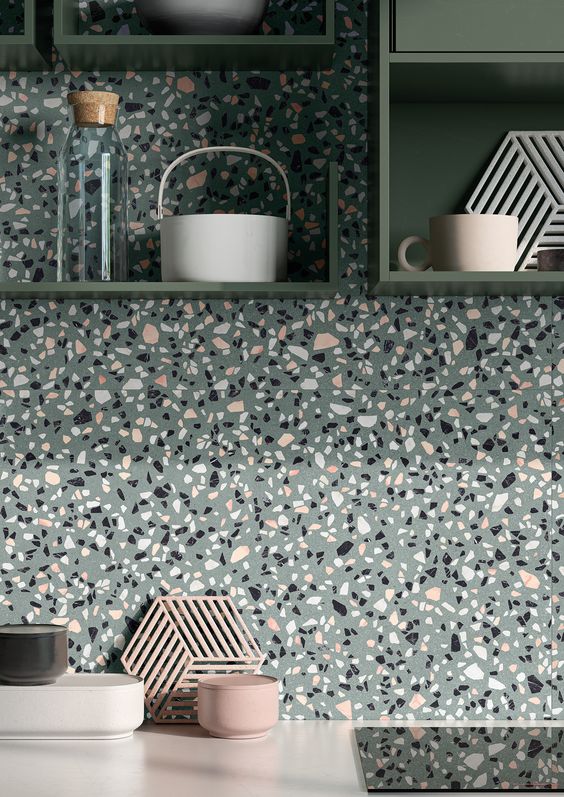 A beautiful gray terrazzo backsplash that matches green shelves and white countertops and looks cool and bright