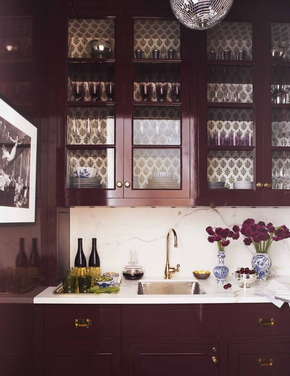 A gorgeous purple kitchen with a white stone backsplash and countertop, gold accents, and a disco ball pendant lamp