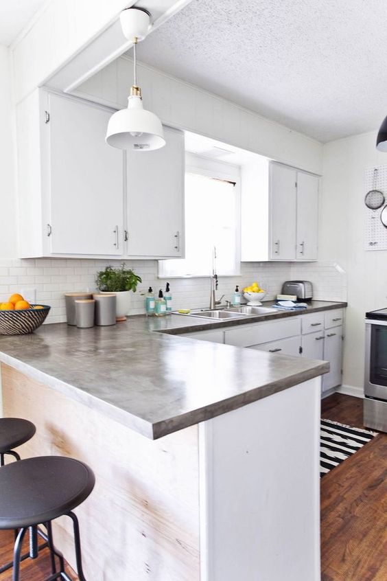 A modern white kitchen with concrete countertops, a white tile backsplash and black handles is chic