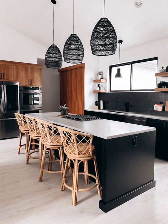 A beautiful black kitchen with a black thin tiled backsplash, white countertops, wicker stools and lamps