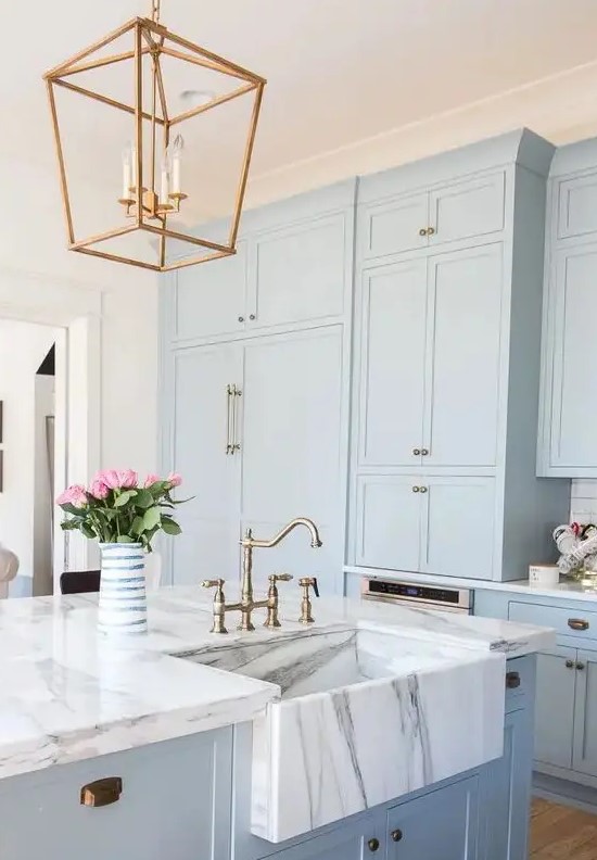 A calm blue kitchen cabinet with white marble countertops and brass accents for a retro look