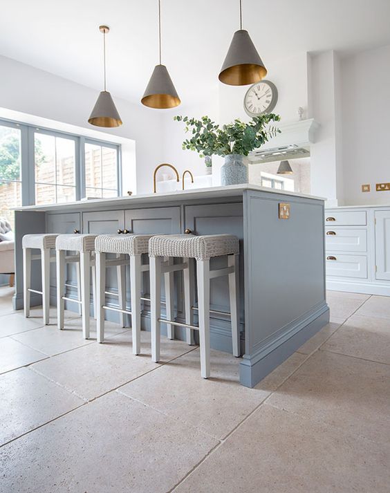 an airy kitchen with light blue cabinets, a blue kitchen island, gray pendant lamps and cream stools