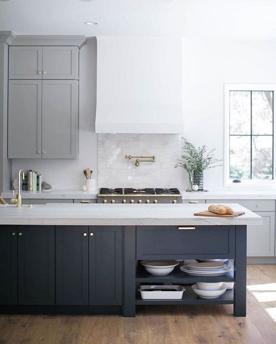 a beautiful and airy modern kitchen with gray cabinets, a white range hood, a navy blue kitchen island with a stone countertop and gold accents