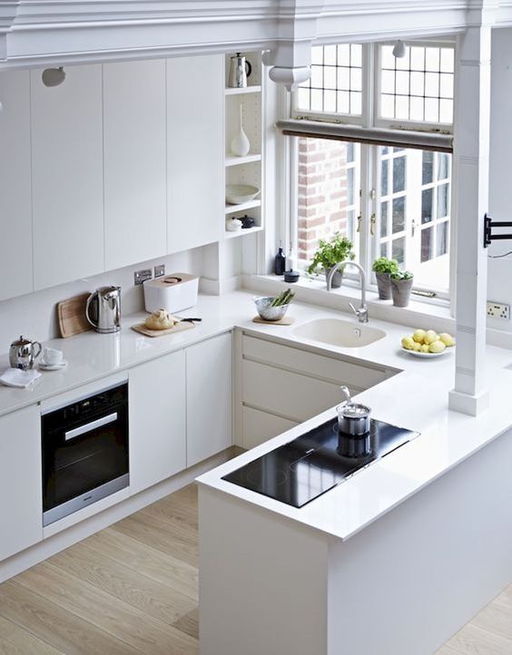 a white, minimalist kitchen with elegant cabinets, no handles, a window and simple built-in appliances