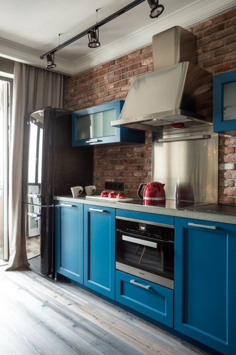 a bold blue kitchen with dark accents and a red brick backsplash and shiny metal accents