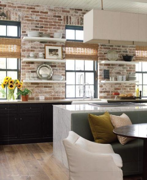 a black kitchen with base cabinets and open shelving, brick walls as a backsplash, a white kitchen island and a pendant lamp
