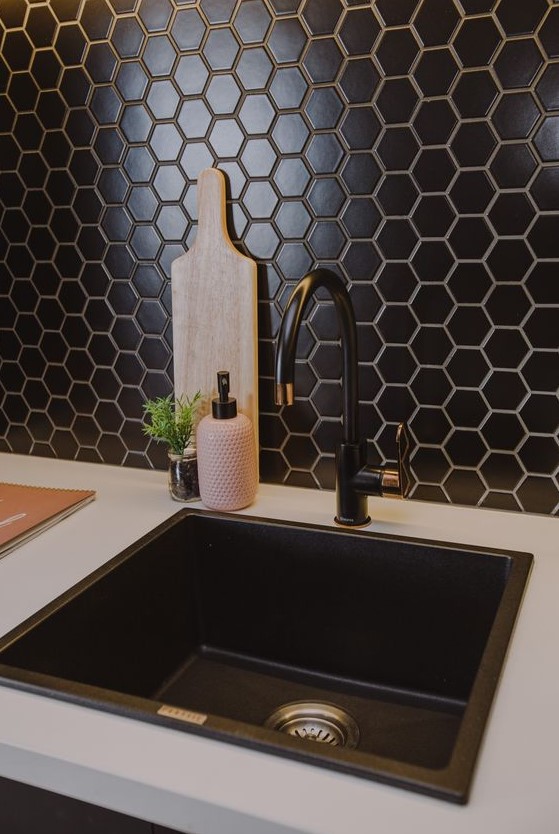 A beautiful and textured backsplash made of black hexagonal tiles adds chic and elegance to the kitchen, and a black sink and taps match it