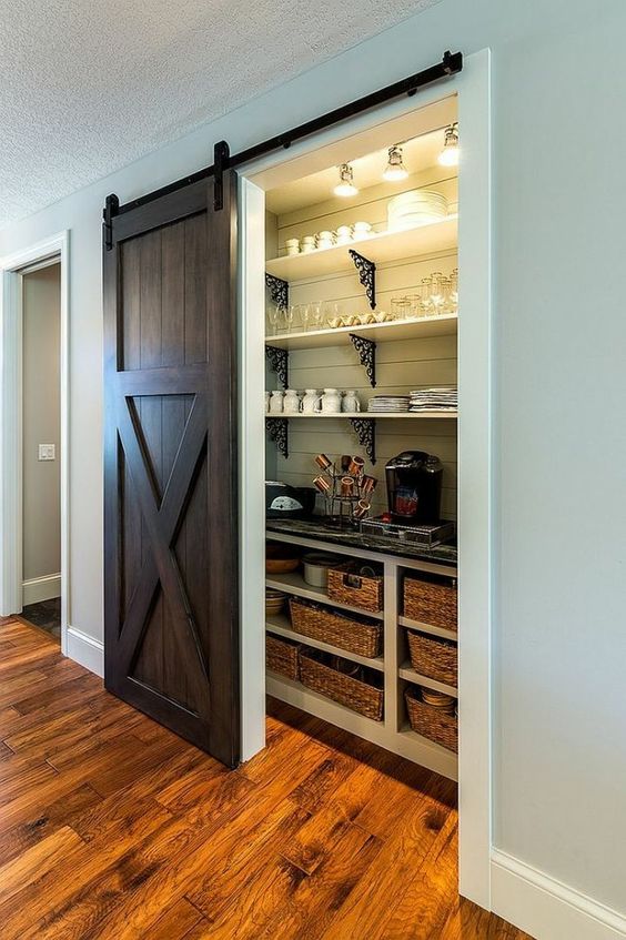 a rustic pantry with a dark stained barn door, open shelves and lights, baskets and various things for a rustic kitchen