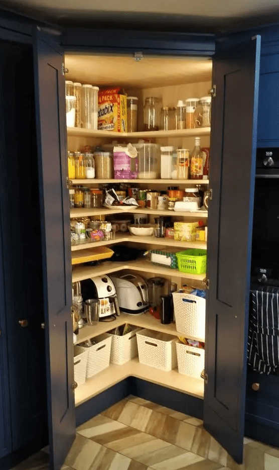 a small pantry built into the kitchen with navy doors, open corner shelves, cubbies and lots of jars and containers, as well as built-in lights