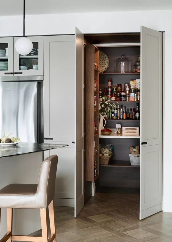 A small pantry that blends into the kitchen, with doors, open shelving and a shelf for spices, as well as some lights