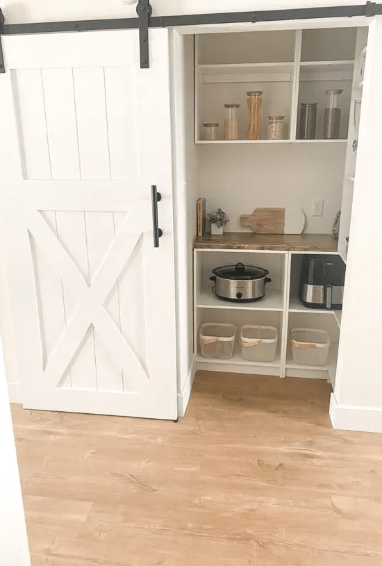 A small pantry with a barn door, open storage units, cookware and shelves is a cool solution for a rustic space