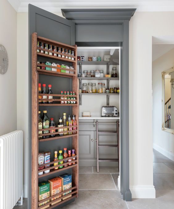 a small pantry with a gray door housing storage shelves and with open shelves and cabinets inside