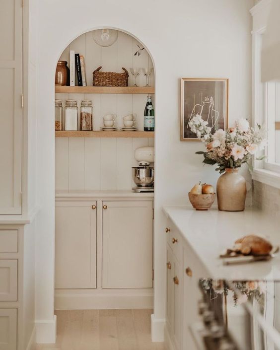 A small pantry with an arched entry, open shelving, and pink cabinets is an elegant storage space that feels cohesive