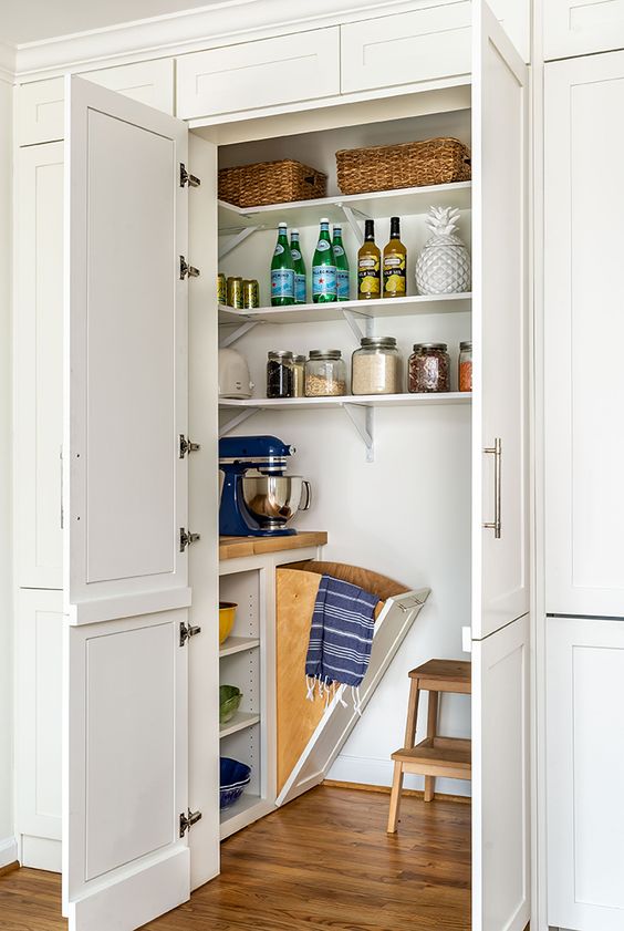 a small pantry with doors, open shelves, a single cupboard and many items and appliances stored in it