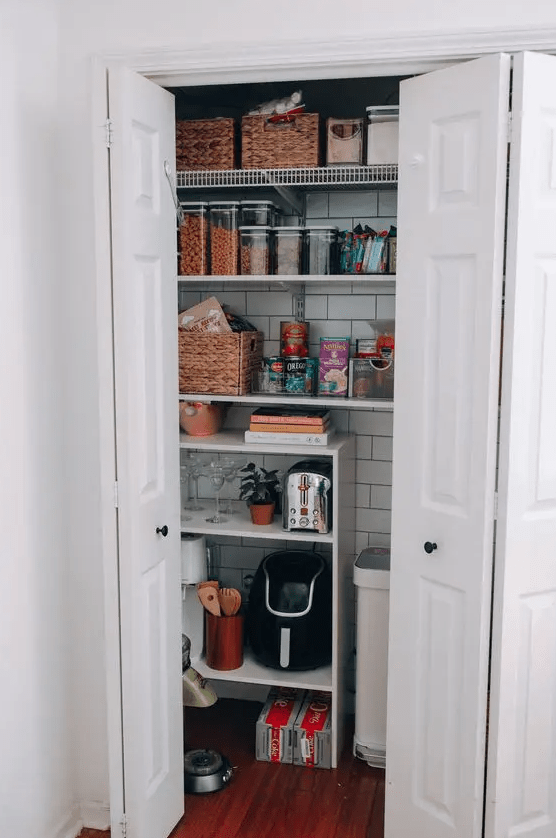 a small pantry with open shelves, a subway tile back wall, cubbies and baskets for storage, and some appliances and groceries