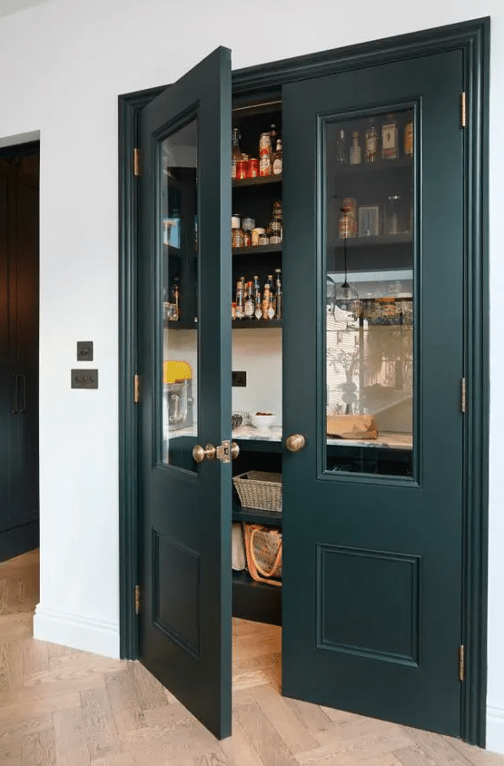 an elegant little pantry with dark green doors, open shelves and baskets, food, drinks and spices