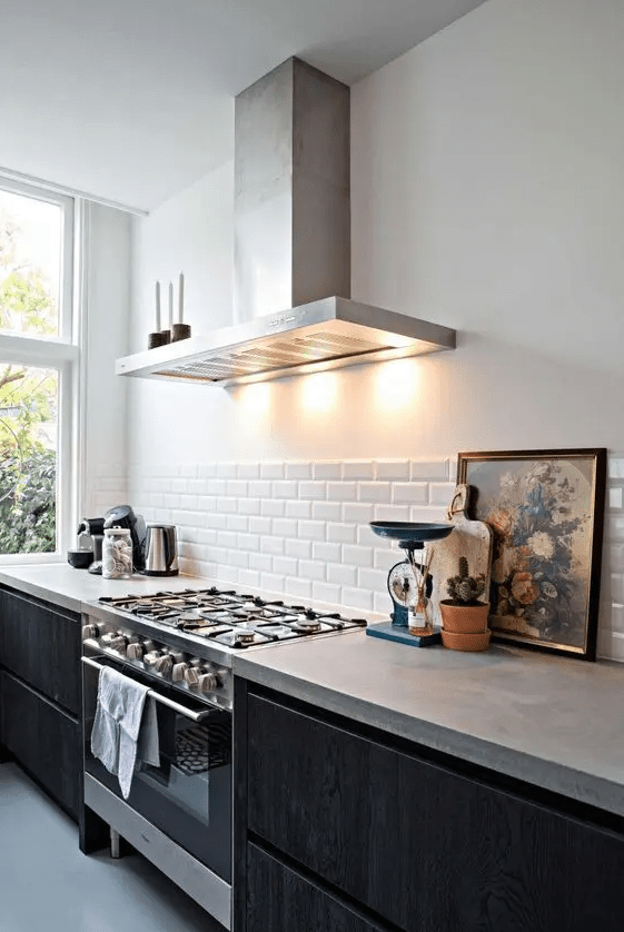 a chic, modern kitchen with black base cabinets and concrete countertops, a white subway tile backsplash and some decor