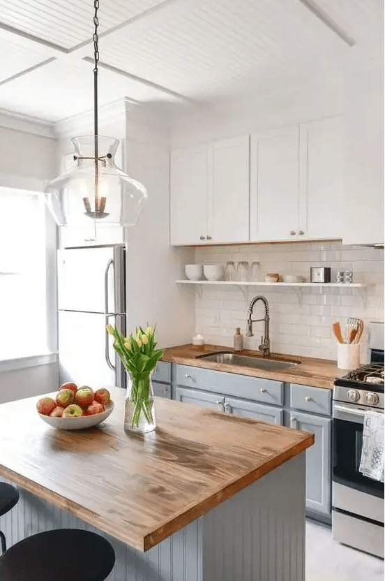 a modern farmhouse kitchen with white and light gray cabinets, butcher block countertops, a glossy subway tile backsplash, and a pendant lamp