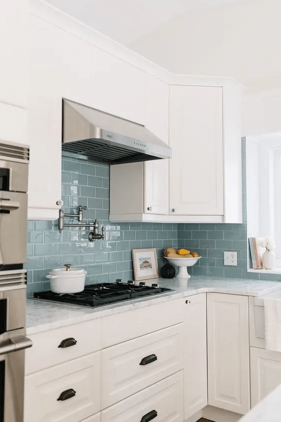 a neutral farmhouse kitchen with shaker cabinets, a blue subway tile backsplash and a metal hood, and white stone countertops