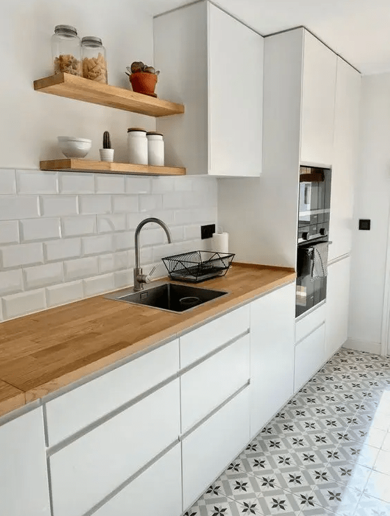 A simple white Scandi kitchen with sleek cabinets, butcher block countertops and a white subway tile backsplash