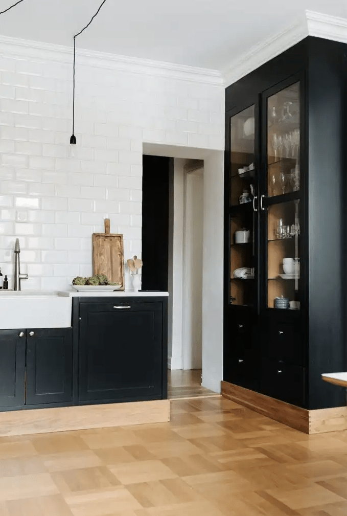 a sleek kitchen with hardwood floors, black shaker cabinets, and white subway tile on the wall