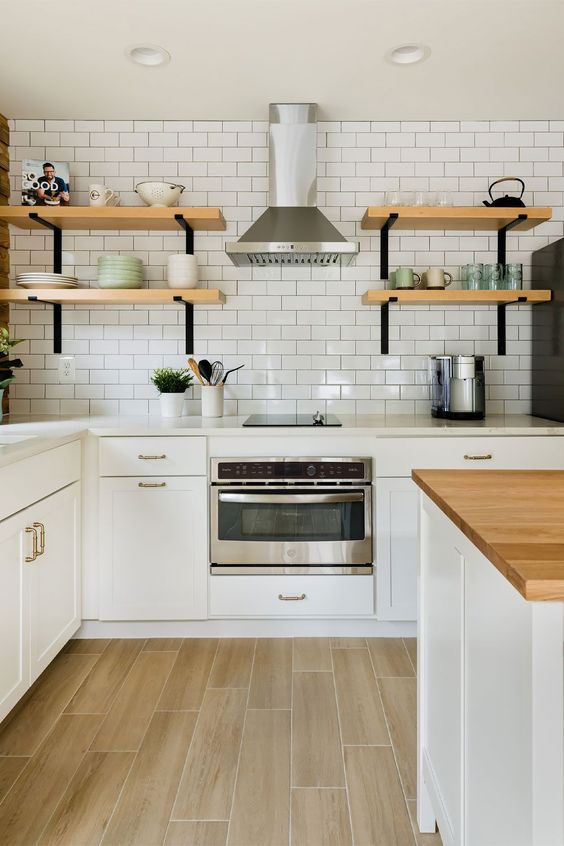 a stylish white Scandinavian kitchen with shaker cabinets, stone and butcher block countertops, a white subway tile wall and shelves