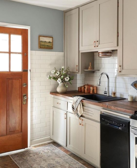 a tan farmhouse kitchen with shaker cabinets, butcher block countertops, brass handles, and white subway tile on two walls